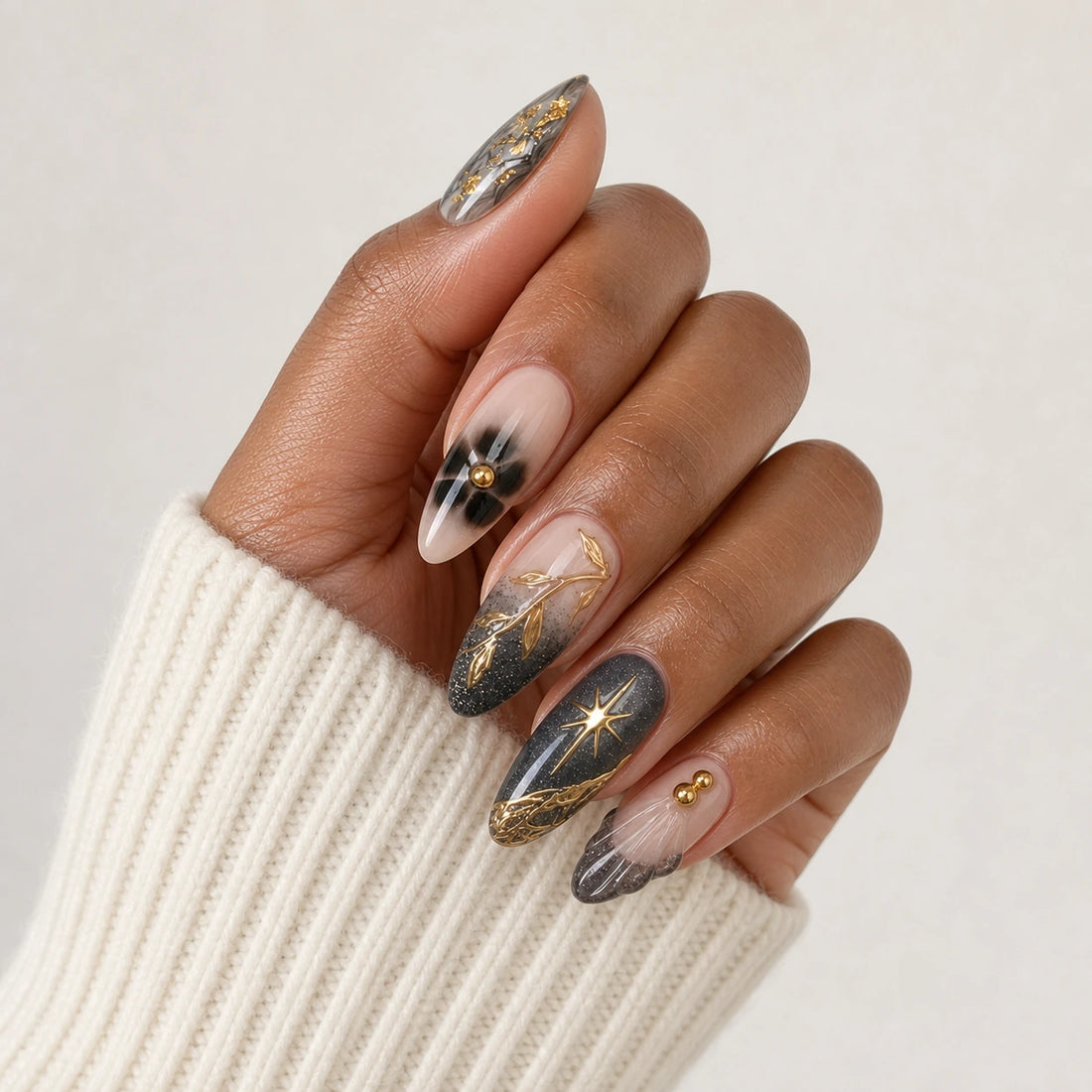 Astral Petal charcoal blush and gold medium almond manicure on one medium-brown hand