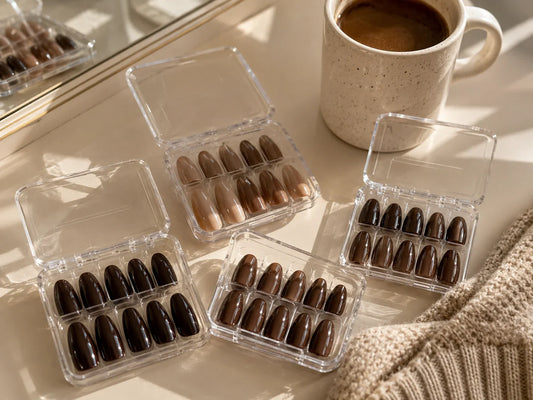 Brown and mocha press-on nails in clear plastic cases beside coffee and knitwear
