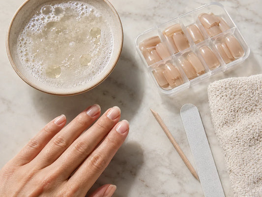 Gentle press-on nail removal setup with warm soapy water, towel and reusable nail box