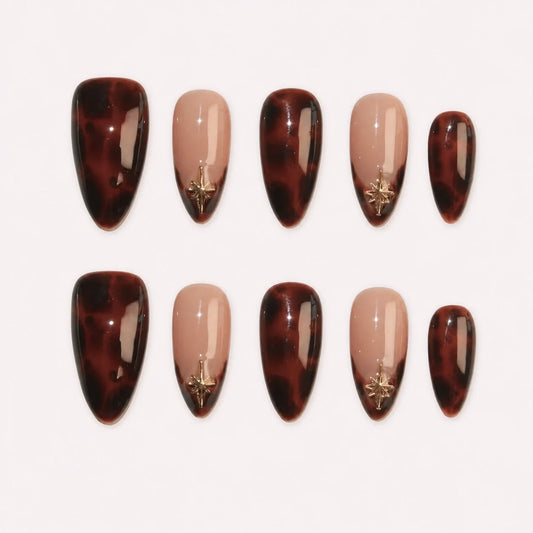 Amber Orbit medium almond press-on nails in glossy tortoiseshell brown and nude with small gold starbursts