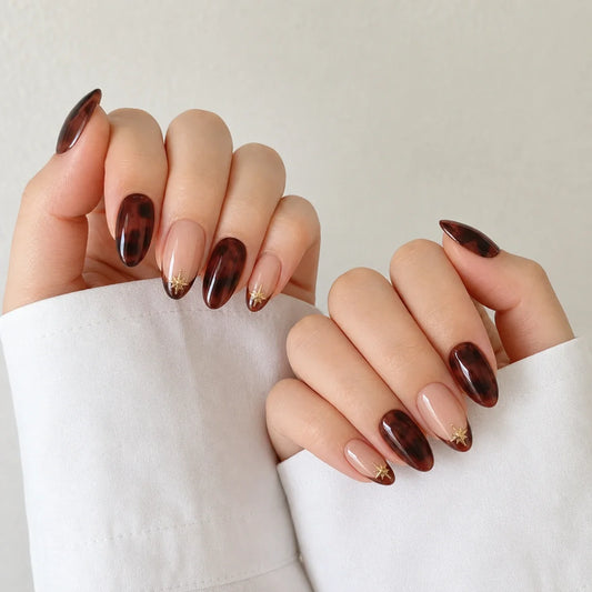 Amber Orbit tortoiseshell and gold starburst press-on manicure on two softly curled hands
