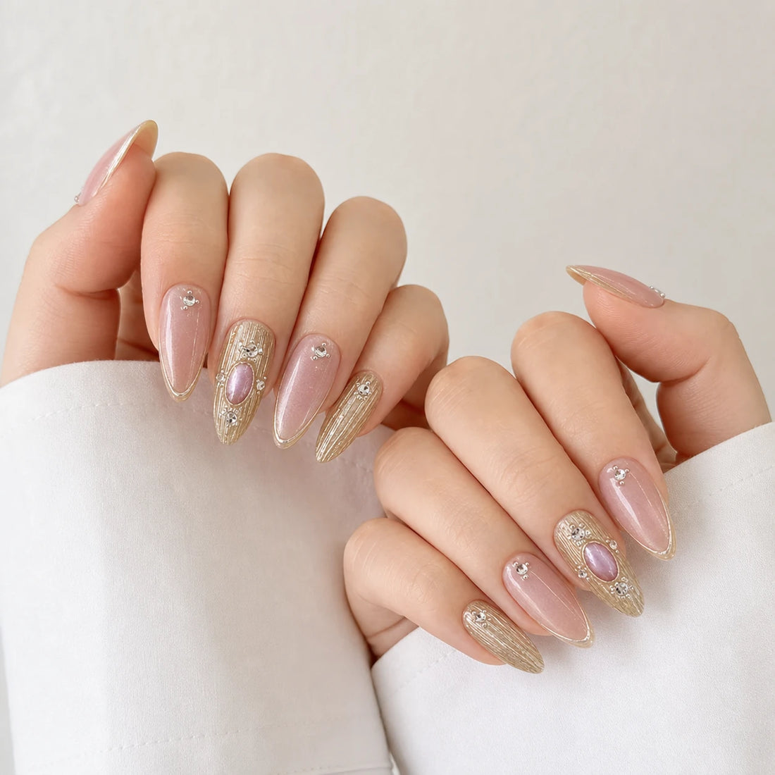 Champagne Oracle pink and gold cabochon manicure on two softly curled light-skinned hands