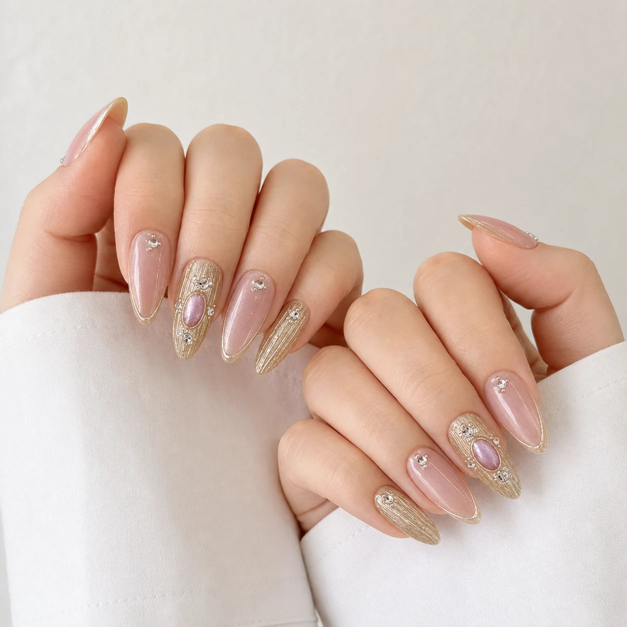 Champagne Oracle pink and gold cabochon manicure on two softly curled light-skinned hands