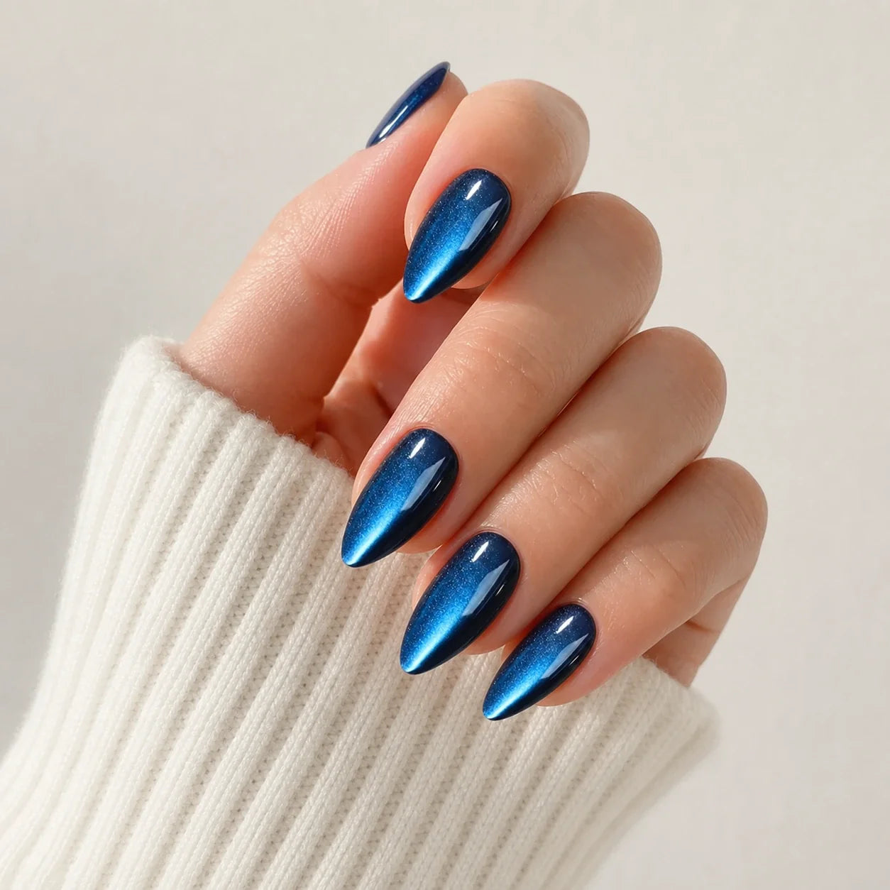 Cobalt Comet blue cat-eye medium almond press-on nails on one softly curled hand