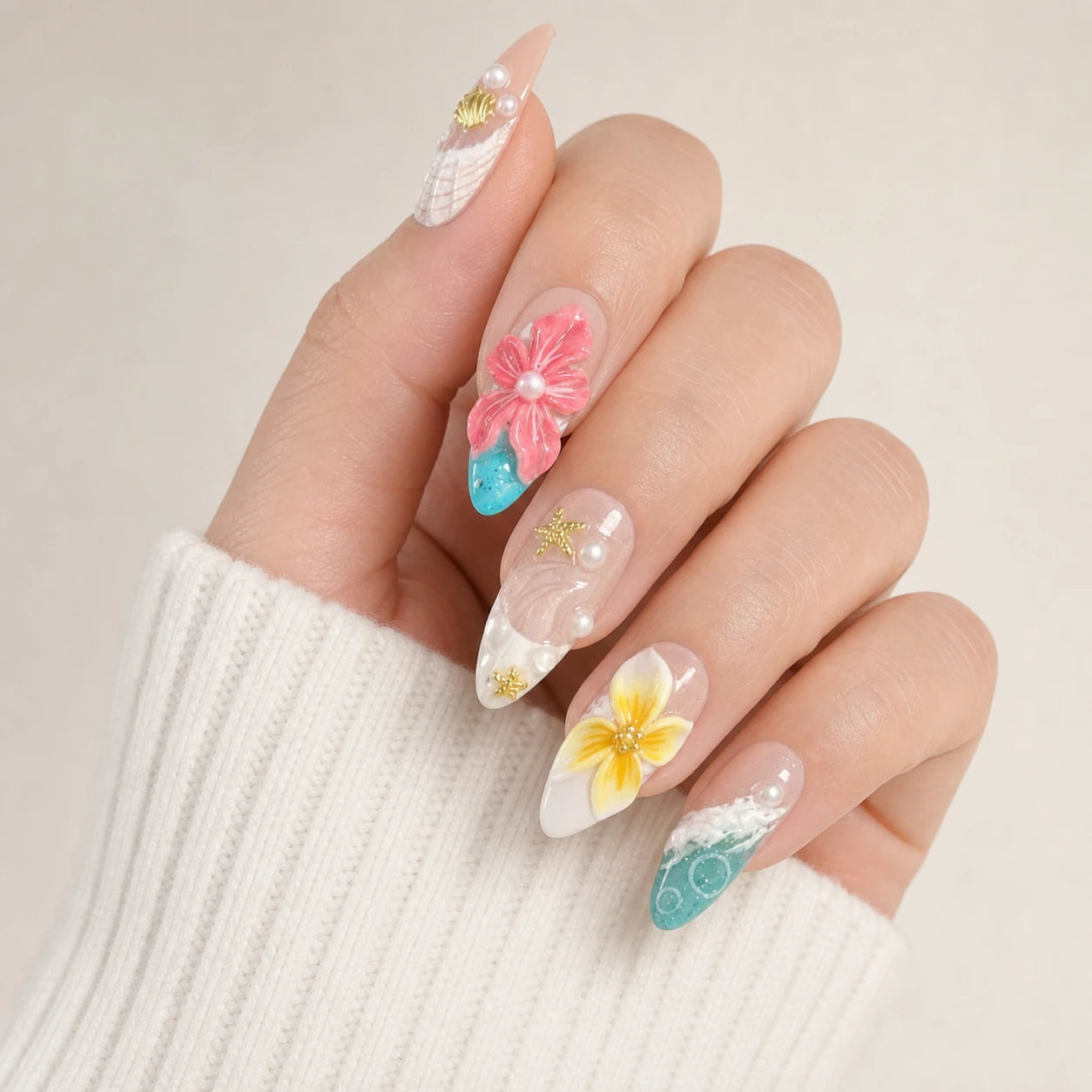 Coral Cabana shell pearl and plumeria manicure on one curled light-skinned hand