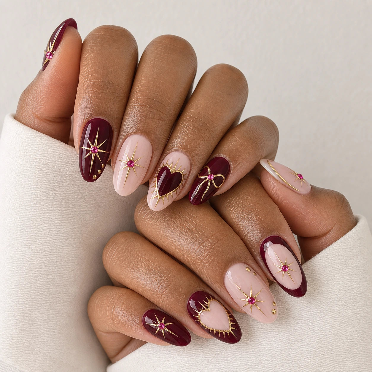 Garnet Wish burgundy blush and gold oval manicure on two medium-brown hands