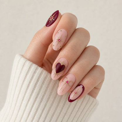 Garnet Wish burgundy blush star bow and heart nails on one curled light-skinned hand