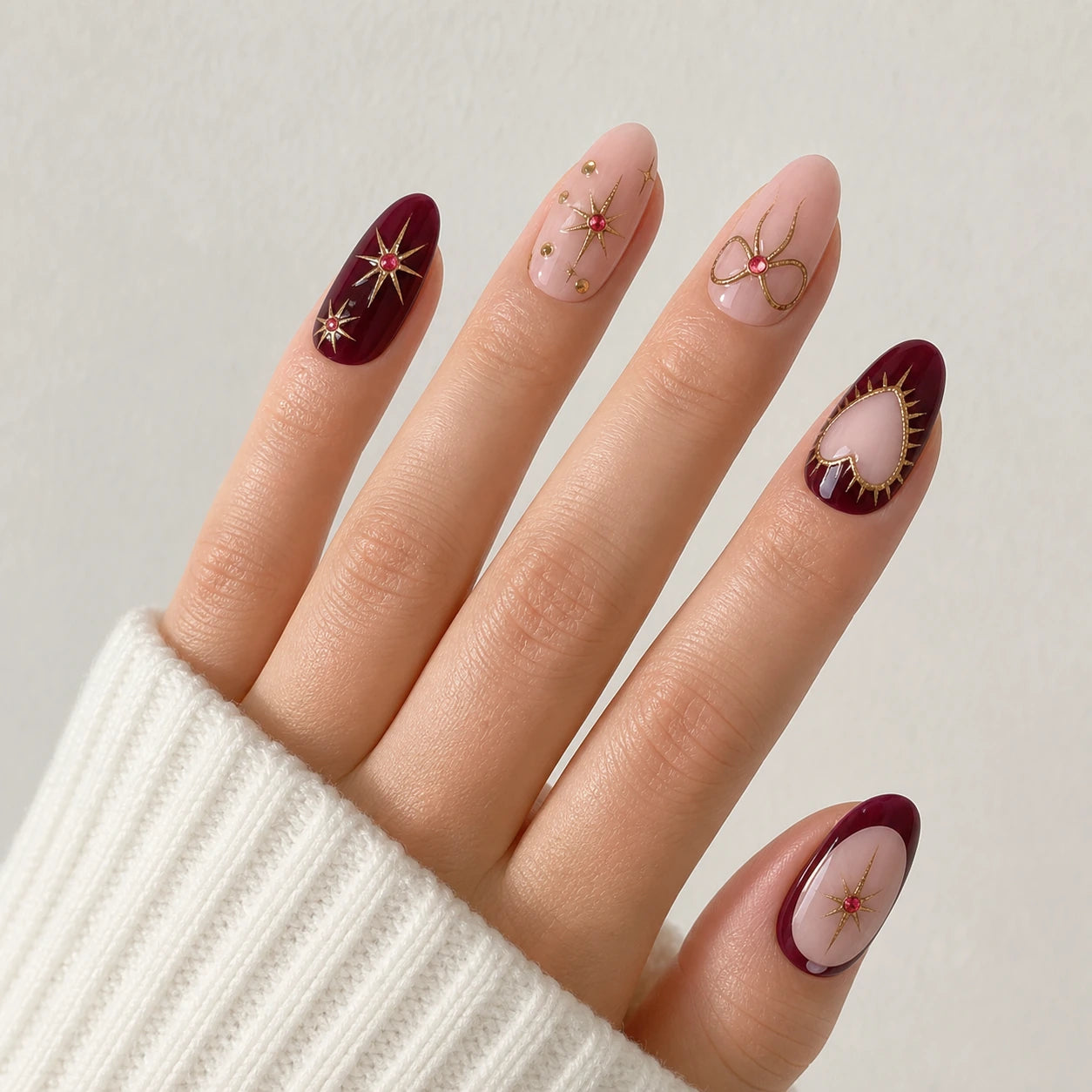 Garnet Wish burgundy blush and gold oval nails on one open light-skinned hand