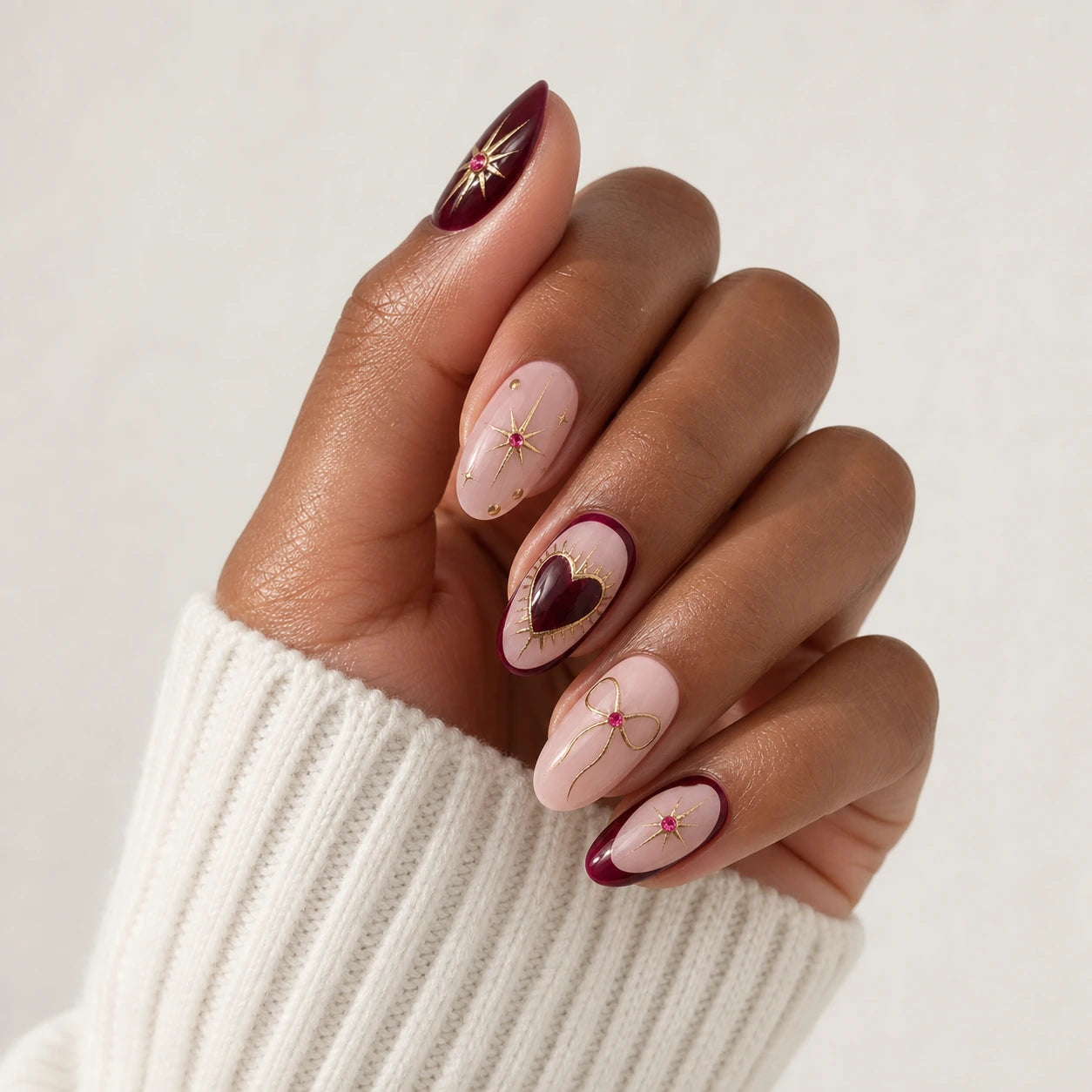 Garnet Wish burgundy blush heart and bow manicure on one medium-brown hand