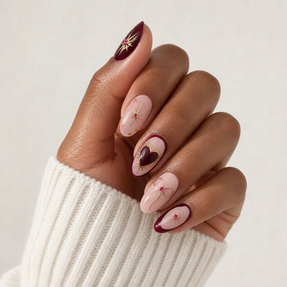 Garnet Wish burgundy blush heart and bow manicure on one medium-brown hand