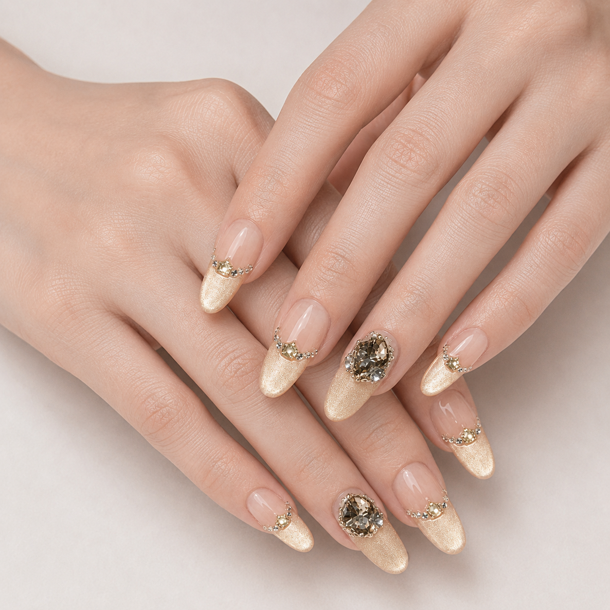 Two crossed hands wearing Gilded Cadence nude peach Long Oval press-on nails with champagne shimmer and smoky crystals