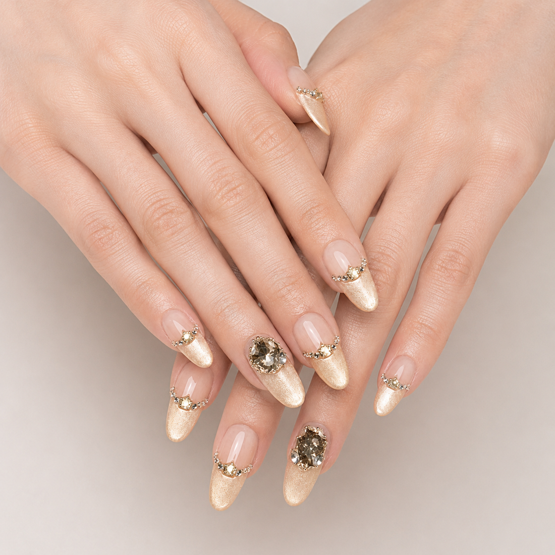 Layered hands presenting Gilded Cadence Long Oval press-on nails with gold cat-eye tips and crystal detailing
