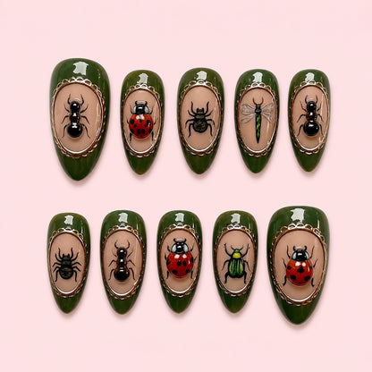 Beetle Cabinet is a 24-piece handmade medium almond press-on nail set in dark olive green, taupe, black and ladybird red, featuring ant, beetle, ladybird and dragonfly studies framed with metallic outlines. It is designed as a reusable multi-size at-home manicure with no selectable size variant, flat lay