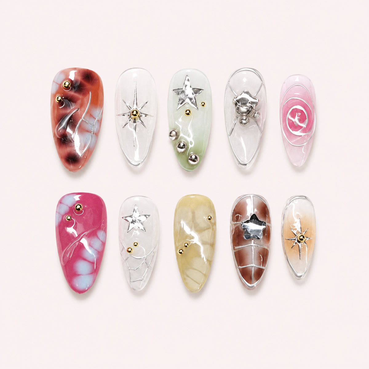 Cosmic Rosette press-on nails with translucent pink, green, yellow and brown tortoiseshell tones, metallic stars, silver swirls and gold beads, flat lay