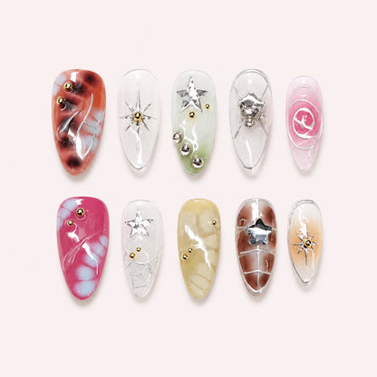 Cosmic Rosette press-on nails with translucent pink, green, yellow and brown tortoiseshell tones, metallic stars, silver swirls and gold beads, flat lay