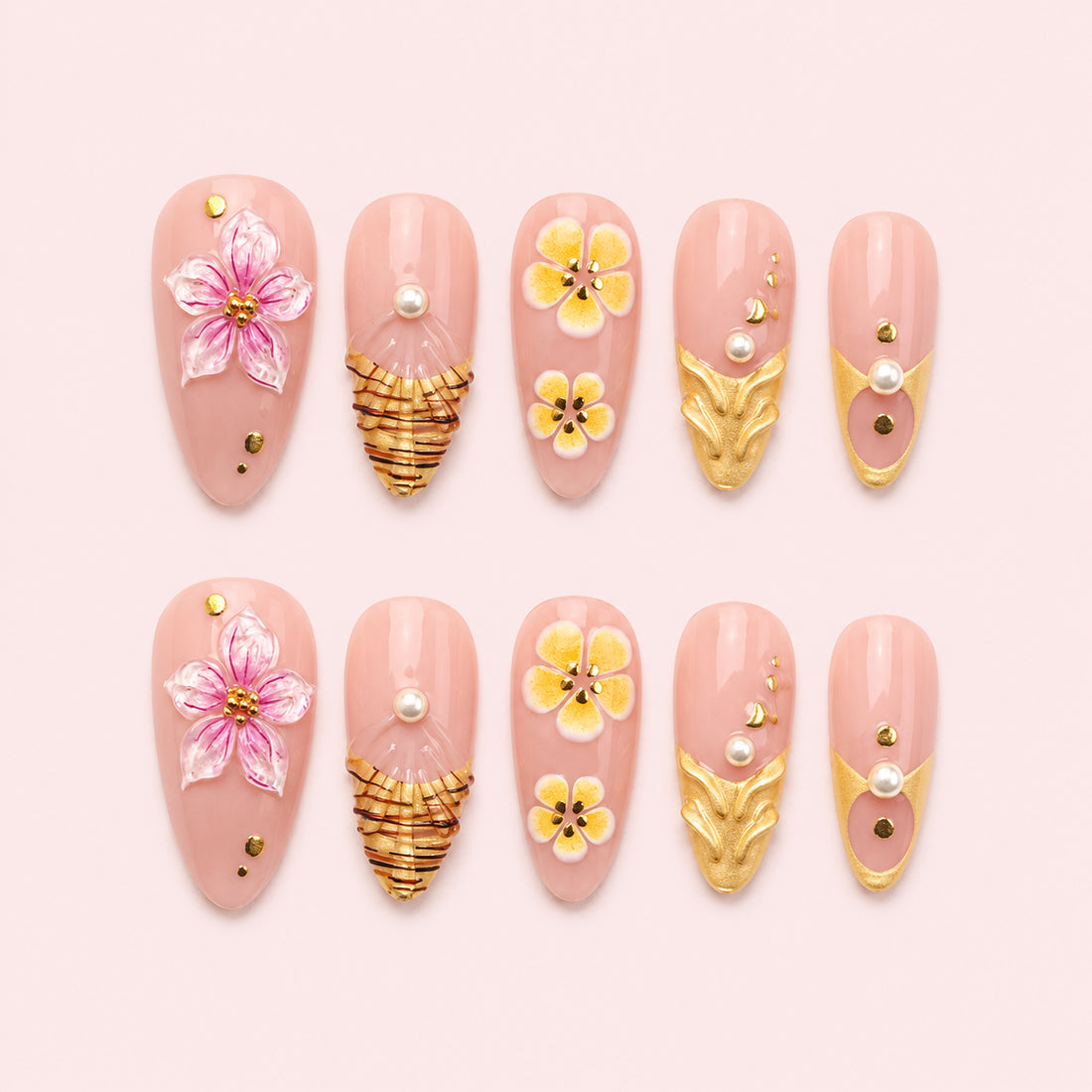 Gilded Hibiscus is a 24-piece handmade medium almond press-on nail set in blush pink, petal pink, yellow and gold, featuring raised flowers, sculptural gold leaves, fan-like gold linework, pearls and studs. It is designed as a reusable multi-size at-home manicure with no selectable size variant, flat lay