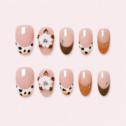 Spotted Magnolia is a handmade glossy short almond press-on nail set in beige, brown, black, white, featuring cow and leopard-style tips with white flowers, flat lay