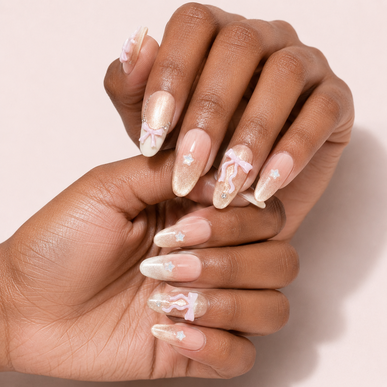 Two curled hands wearing Ribbon Constellation Long Oval press-on nails with rhinestones and bows